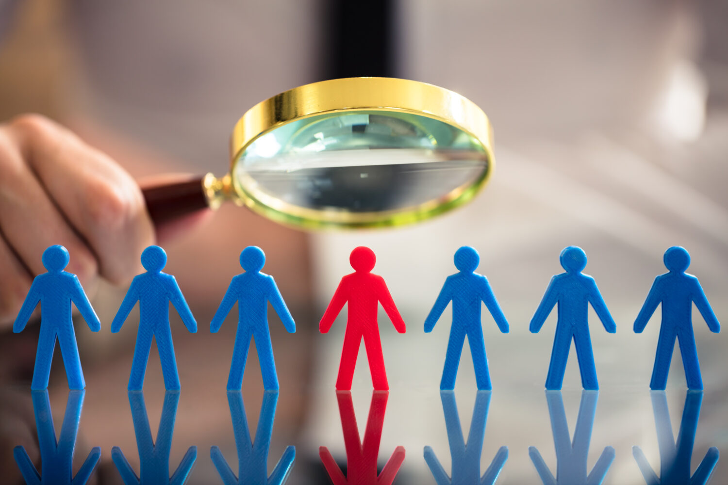 A person's Hand Holding Magnifying Glass Over Red Human Figure Standing Amongst Blue Figures. Abolishing the U.S. Department of Education