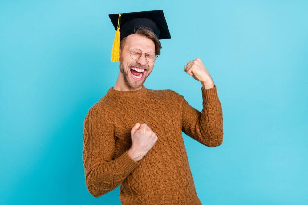 Photo of funny adorable guy dressed knit sweater academic hat spectacles screaming rising fists isolated blue color background