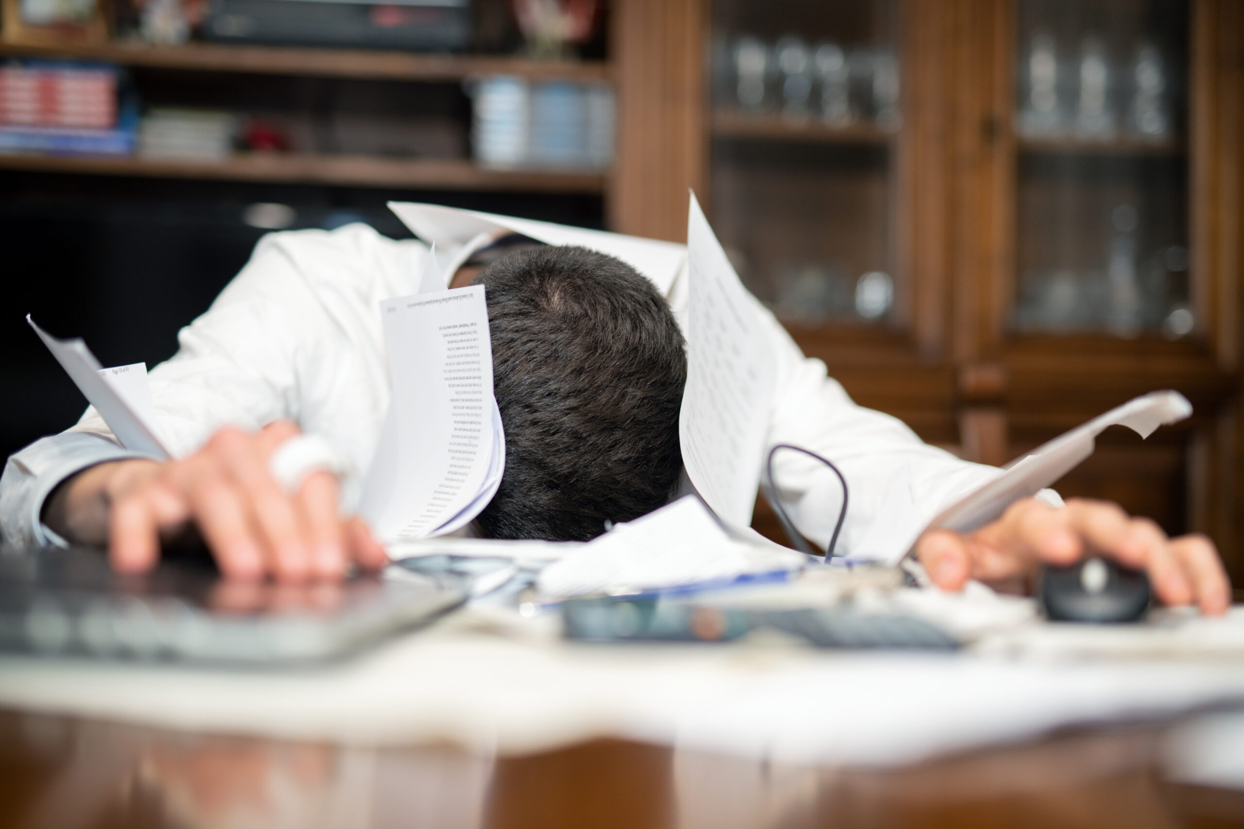 Desperate man submerged with student loan papers, delinquent bills, and labtop with head down on them.